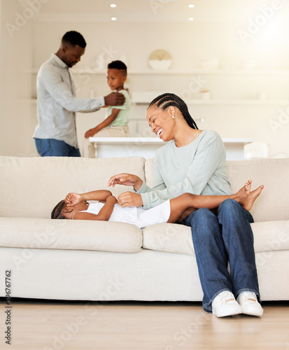 Beautiful young african american mom bonding with her daughter on the sofa in their living room at home. Black woman playing with her adorable little girl at home. Dad and his son in the background