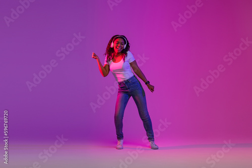 Feel The Beat. Black Woman In Wireless Headphones Dancing In Neon Light
