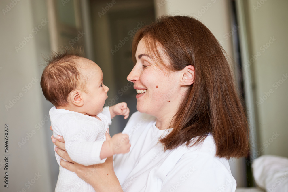 Mother playing with her newborn baby. Home portrait of newborn baby and mother. Enjoying time together