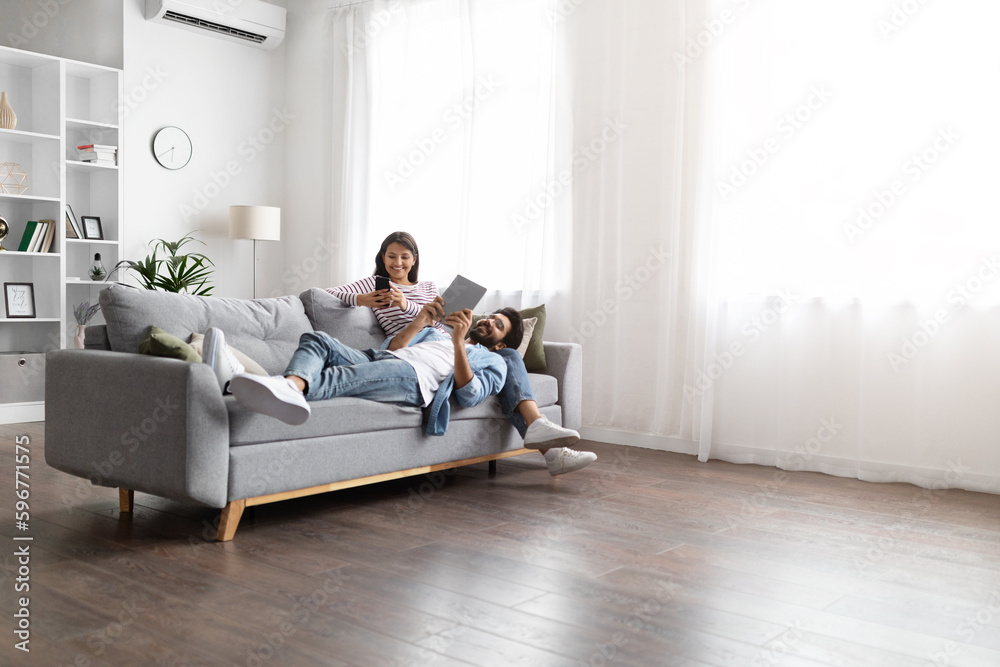 Candid shot of eastern couple chilling on couch, using gadgets Candid shot of eastern couple chilling on couch, using gadgets