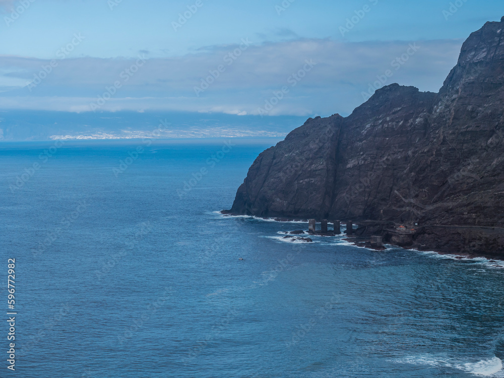 View of Tenerife island and Pescante de Hermigua, concrete pillars and ruins of old port, former loading station for banana tomato export on ocean coast. Hermigua, La Gomera, Canary islands, Spain