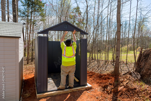 Worker is putting together plastic vinyl storage shed for backyard nearby