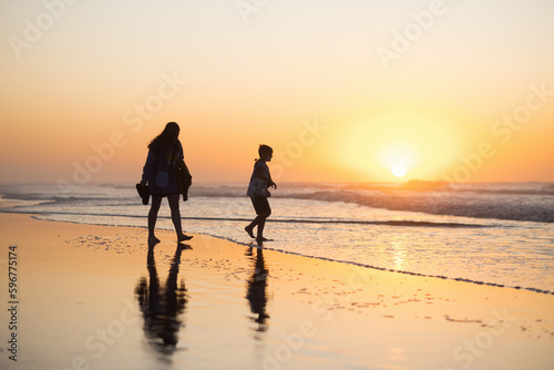 Madre e hijo caminando en la playa durante el atardecer
