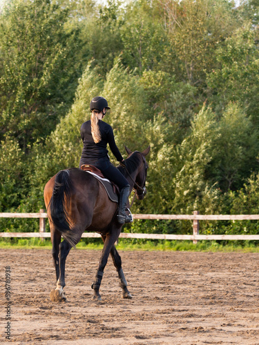 Back view of blond young woman riding brown horse in enclosure, Quebec City, Quebec, Canada