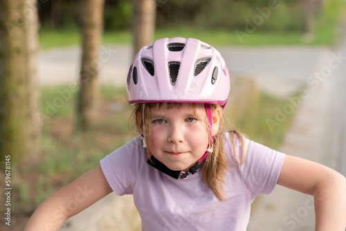 Young girl biker school age child wearing a protective helmet, focused cyclist kid outdoors portrait, face closeup, copy space, blurred background. Sports, physical activity safety concept, one person © Tomasz