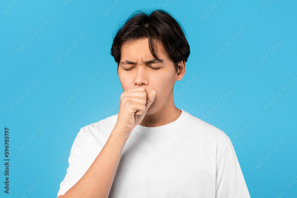 Sick Asian Teen Guy Coughing In Fist Over Blue Background Sick Asian Teen Guy Coughing In Fist Over Blue Background