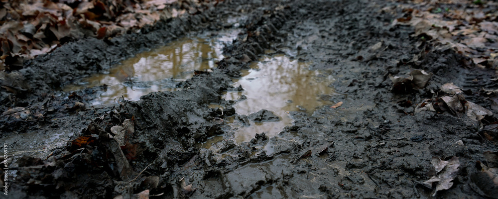 Fototapeta premium Muddy rural road with large puddle with dirty brown water on farm field in rain season.