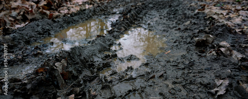 Muddy rural road with large puddle with dirty brown water on farm field in rain season.