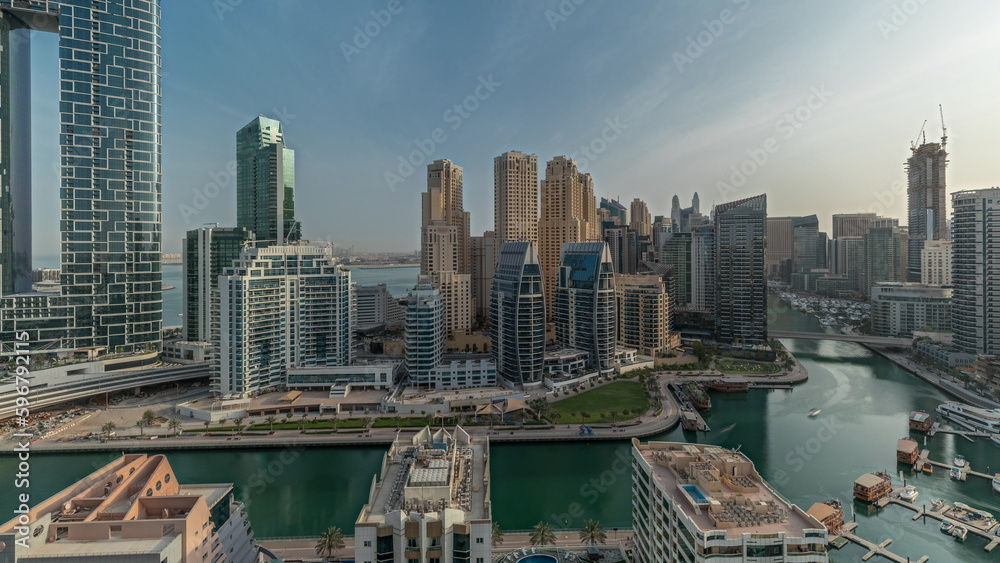 Panorama showing Dubai Marina with several boats and yachts parked in harbor and skyscrapers around canal aerial morning timelapse.