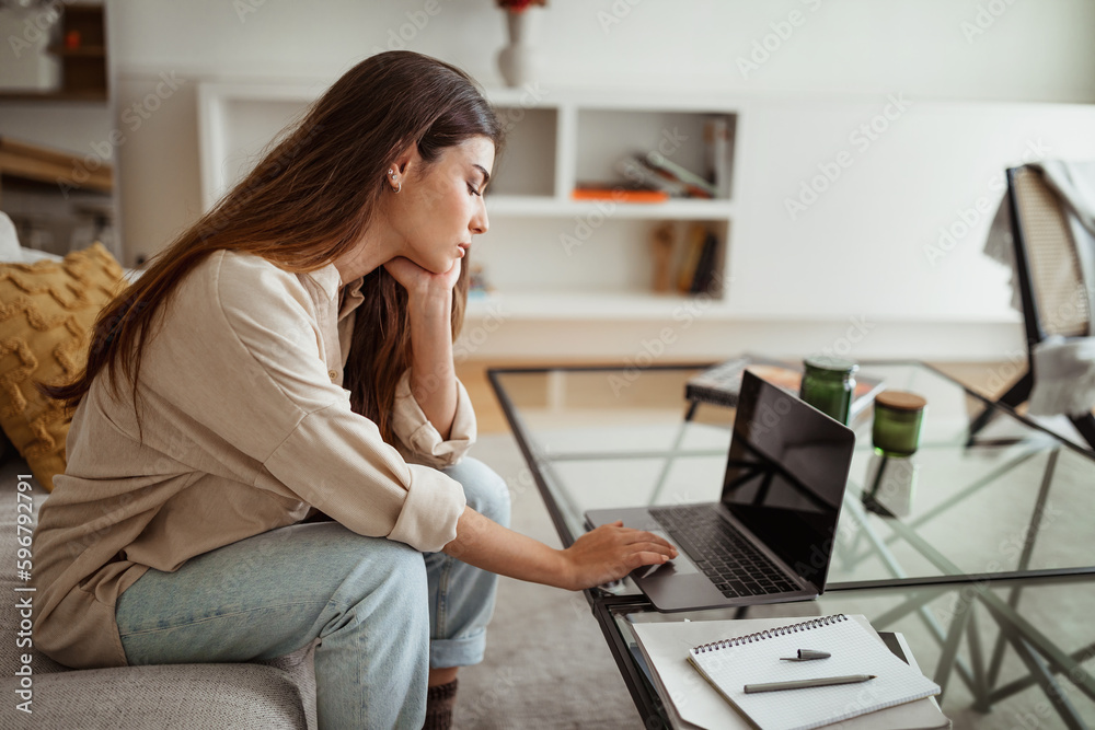 Tired busy boring millennial european female typing on computer in minimalist living room interior, profile