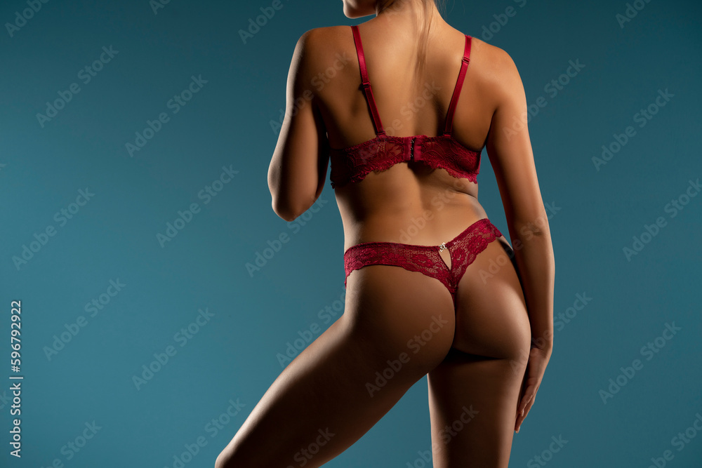 Tanned woman in top form, perfect body shape in the shadow. Parts of woman body in red underwear, back rear view, blue background