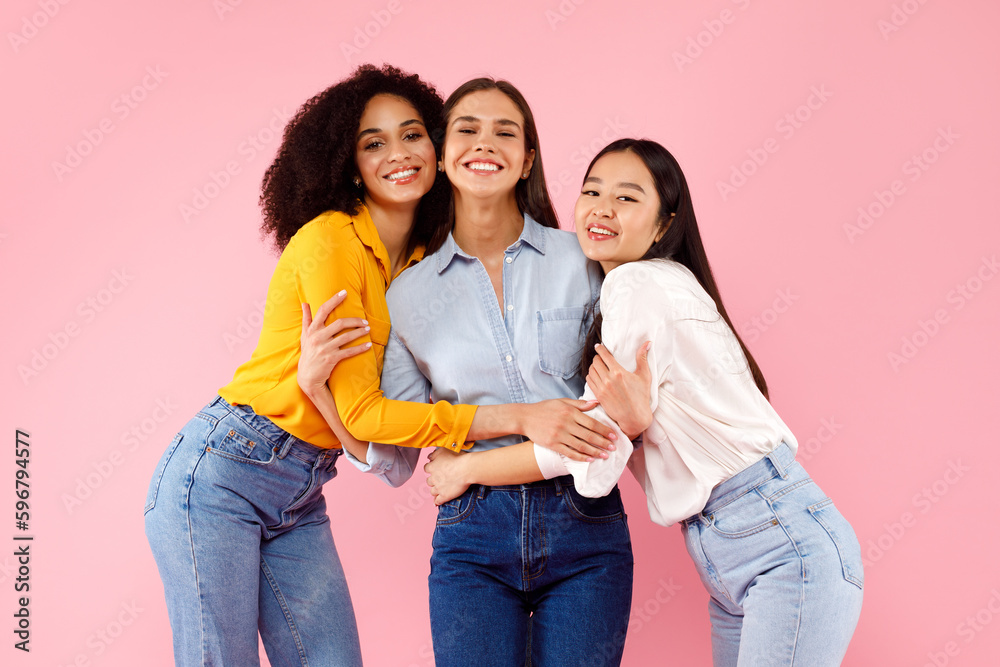 Portrait of three cheerful diverse ladies embracing while posing over pink studio background, smiling at camera Portrait of three cheerful diverse ladies embracing while posing over pink studio background, smiling at camera