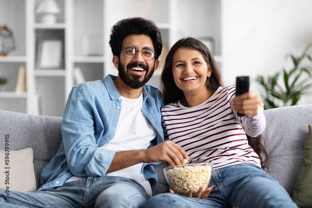 Smiling interracial spouses sitting on couch at home, watching tv Smiling interracial spouses sitting on couch at home, watching tv