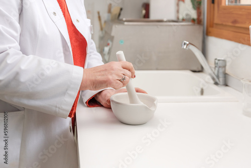 Doctor in medical uniform using mortar and pestle during medical preparation photo