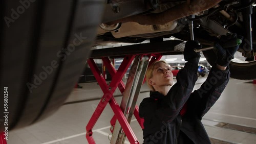 Suspension repair. A female car mechanic stands under the car and unscrews the rear suspension bolts with a wrench