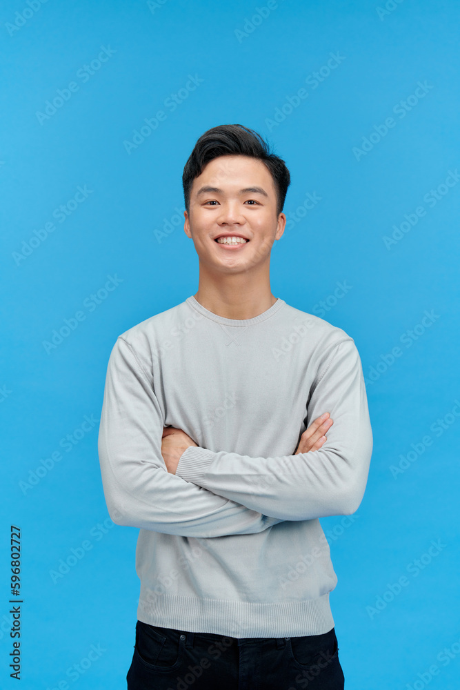 Smiling handsome Asian man with arm crossed looking at camera isolated on blue background Smiling handsome Asian man with arm crossed looking at camera isolated on blue background