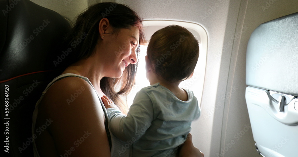 Mother holding baby inside airplane. Parent with infant child traveling by commercial plane