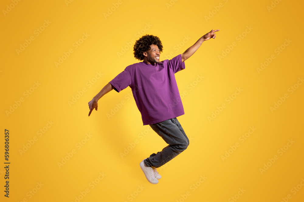 Cheerful adult african american curly man in purple t-shirt dancing, has fun alone