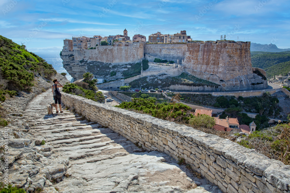 Bonifacio at the edge of the chalk cliff. Women with little dog looks on the old town and the fortress of Bonifacio, Corsica island, France