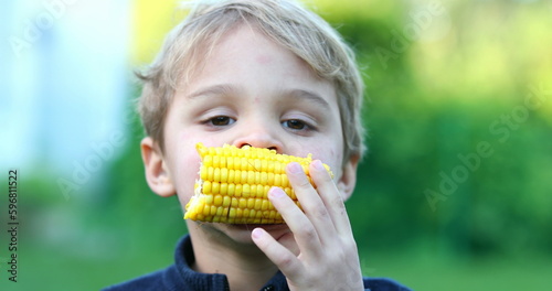 Happy infant toddler eating corn outside. Funny baby boy holding and eating healthy snack