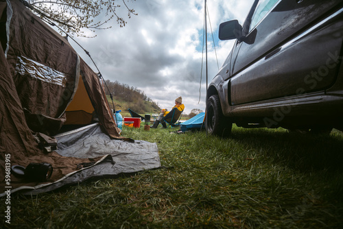 Camping in the wilderness. An off-road vehicle. Tent and equipment for tourism. Travel and vacation, active recreation. A woman is having dinner. Cold weather.