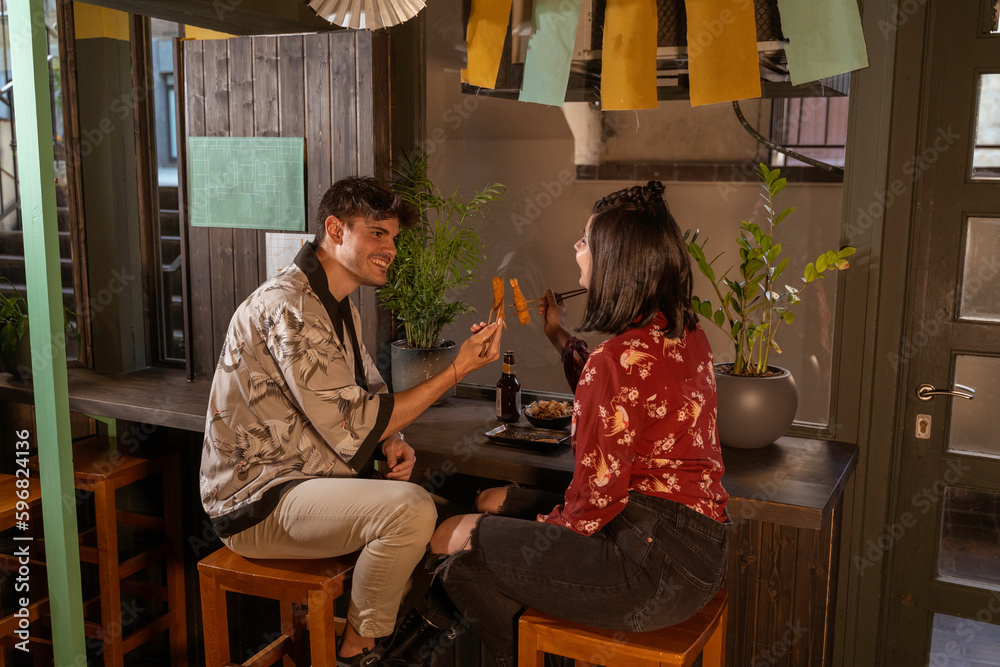 Young romantic couple from Europe. They are dressed in Japanese prints enjoy an oriental meal and clash their chopsticks to celebrate in a Japanese restaurant.