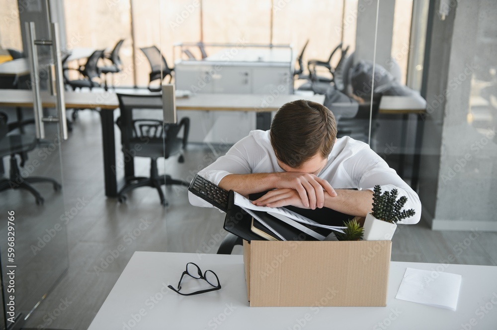 Sad Fired. Let Go Office Worker Packs His Belongings into Cardboard Box and Leaves Office. Workforce Reduction, Downsizing, Reorganization, Restructuring, Outsourcing. Mass Unemployment Market Crisis