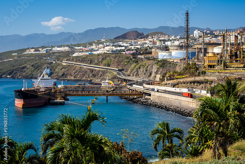 Obraz na plátně Petrochemical industry in Santa Cruz de Tenerife showcasing a refinery plant, moored tanker, towering chimney and pipeline at Honduras harbor while palm trees offer a contrast to the industrial area