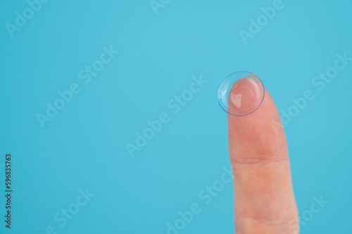 Woman holding contact lens on blue background. 