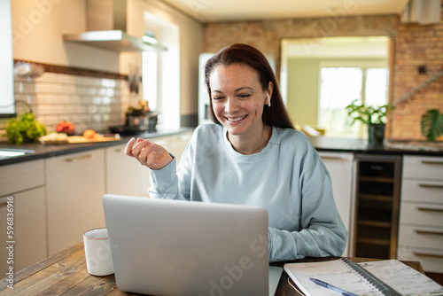 Young adult woman having a video call on a laptop in a kitchen