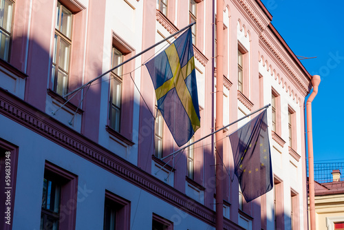 Close-up view of Swedish and EU flags fluttering on pink building wall in the early morning. Clear blue sky. Soft focus. Travel in Scandinavia theme. photo