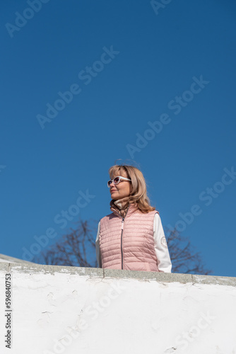 Beautiful adult woman in sunglasses with blond hair on the stairs against a blue clear sky. © Andrey Nikitin