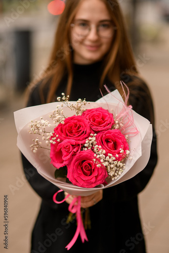 Woman holding luxury composition of fresh red roses, white gypsofila and pink feathers photo