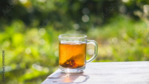 Transparent mug with fresh hot berry black tea and currant. An invigorating drink in the early morning in nature with the rays of the warm sun