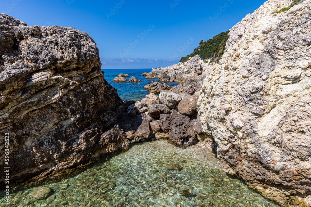 A beautiful landscape of the coast of the island of Corfu in the Ionian Sea of the Mediterranean in Greece. Pure blue clear water washes over the shores of the Greek island.