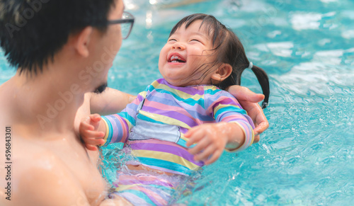 Asian little baby girl swimming in pool, Father holding daughter for safety support, Living lifestyle family indoors concept.