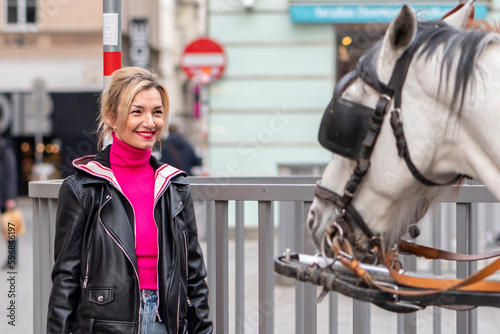 portrait of a blonde woman 35-40 years old, looking at a horse-drawn carriage in a European city. Concept: tourism and travel, horseback riding.
