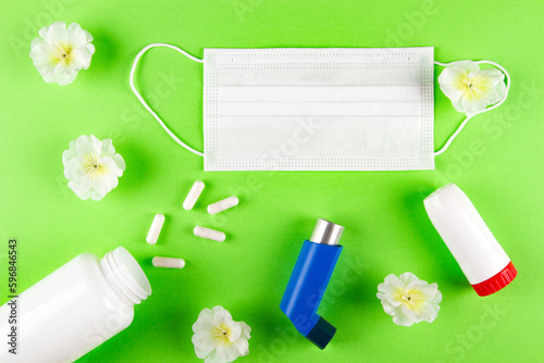 White shurgary mask, white flowers, bottle with pills and inhalers on light green background.  Allergic bronchial reaction Concept photo