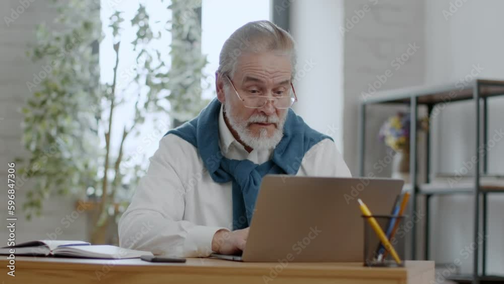 Senior man wearing eyeglasses networking on laptop and getting win message, laughing and celebrating victory at home Senior man wearing eyeglasses networking on laptop and getting win message, laughing and celebrating victory at home