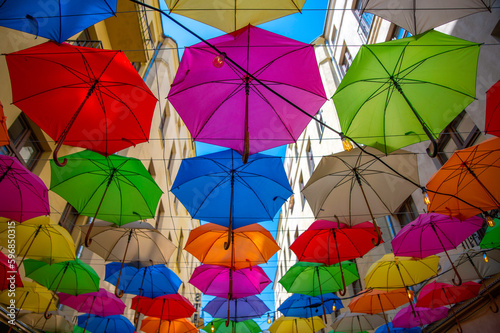 Ulica Piotrkowska w Łodzi i kolorowe parasole wiszące między budynkami nad błękitnym niebem.