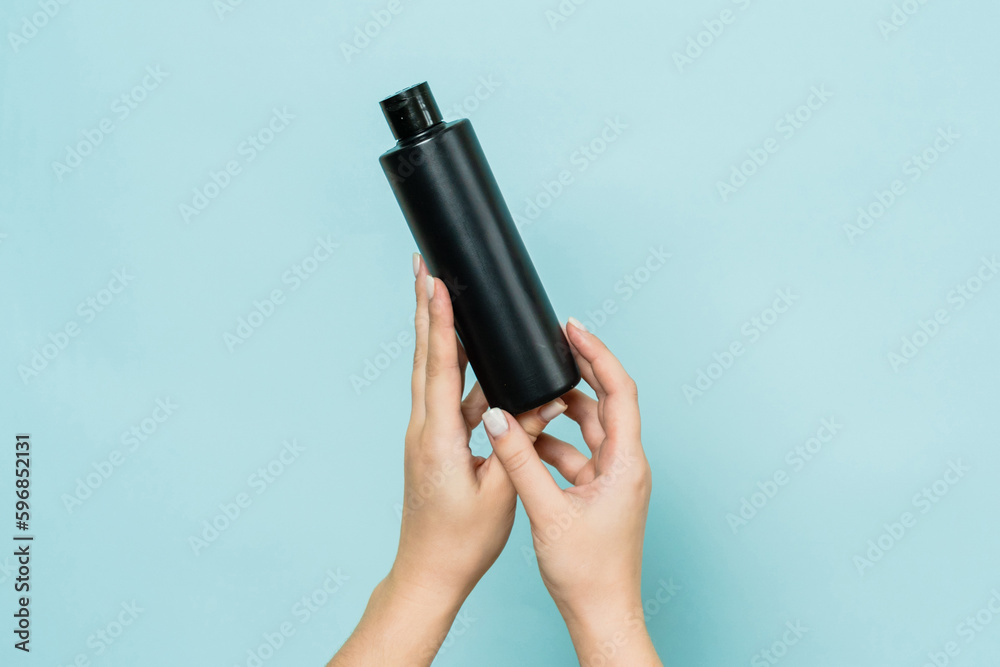 Hands hold black bottle of cosmetic product for skin on blue background Hands hold black bottle of cosmetic product for skin on blue background