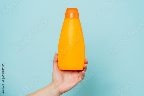 Woman's hand holding packaging of shampoo or conditioner on blue background. Copy space and mock up