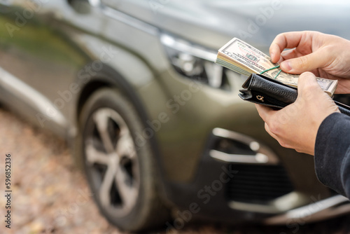 Person holding a wallet in the hands stands front car. Insurance, loan and buying car finance concept