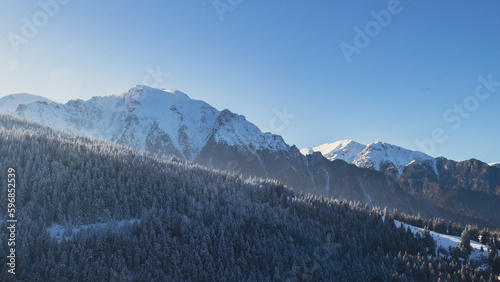 Blue winter landscape in Bucegi Mountains, Diham, with snowy peaks and sunlit pine trees © Radu