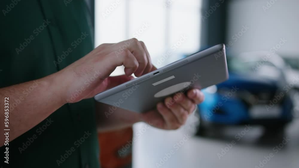 Close-up of the hands of a car sales manager with a tablet against the background of a modern showroom Close-up of the hands of a car sales manager with a tablet against the background of a modern showroom