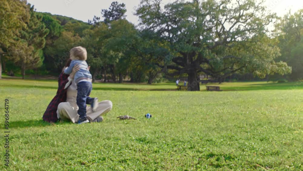 A little boy runs into his mother's arms and drops her on the grass A little boy runs into his mother's arms and drops her on the grass