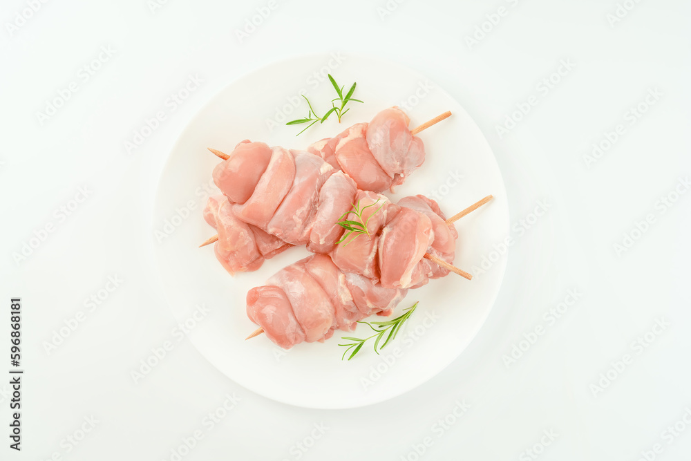 Chicken skewers.Skewers from raw chicken leg meat without skin on a white plate with fresh herbs rosemary for supermarket on a white background.Food for retail.Chicken meat.Procurement for designers. Chicken skewers.Skewers from raw chicken leg meat without skin on a white plate with fresh herbs rosemary for supermarket on a white background.Food for retail.Chicken meat.Procurement for designers.