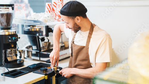 Fotografija Male barista using tamper at espresso machine in coffee shop