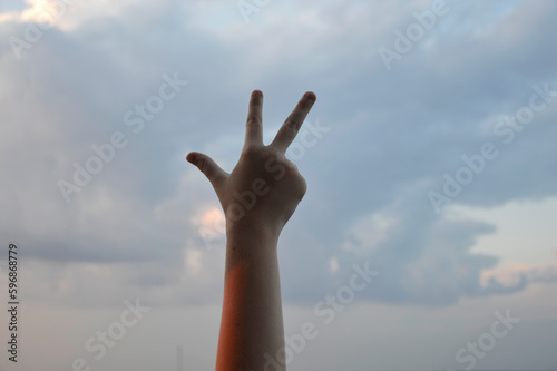 silhouette of a hand, against the background of the sky at sunset, shows a symbol with fingers. message or gestures. silence and beauty in nature
