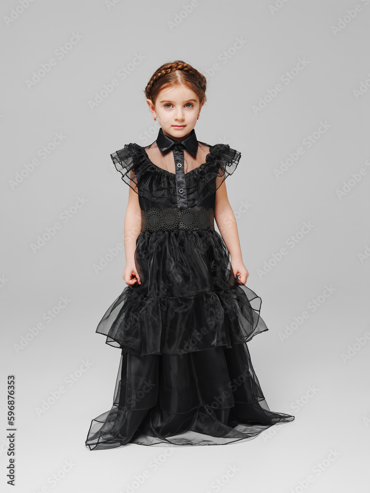 cute little girl with pigtail in a black long curvy dress on a gray background. cute little girl with pigtail in a black long curvy dress on a gray background.
